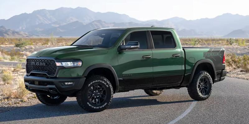 A green RAM 1500 truck parked on a road with a desert landscape and mountains in the background.