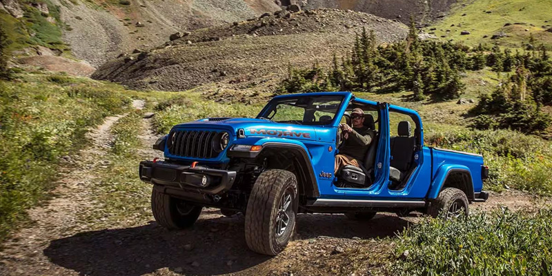 A blue Jeep vehicle driving off-road on a rugged trail, with a person behind the wheel.