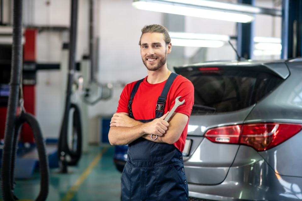 a mechanic stands in a garage holding a wrench