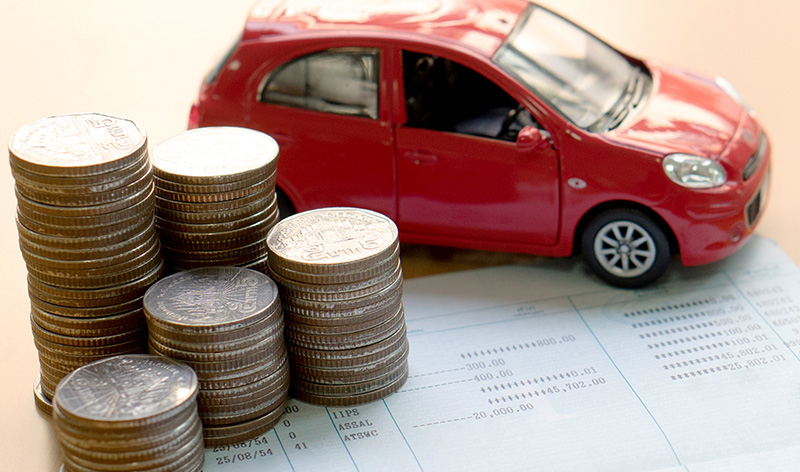 A close-up of a toy red car next to stacks of coins on top of a bank statement, symbolizing financial planning or car-related expenses.