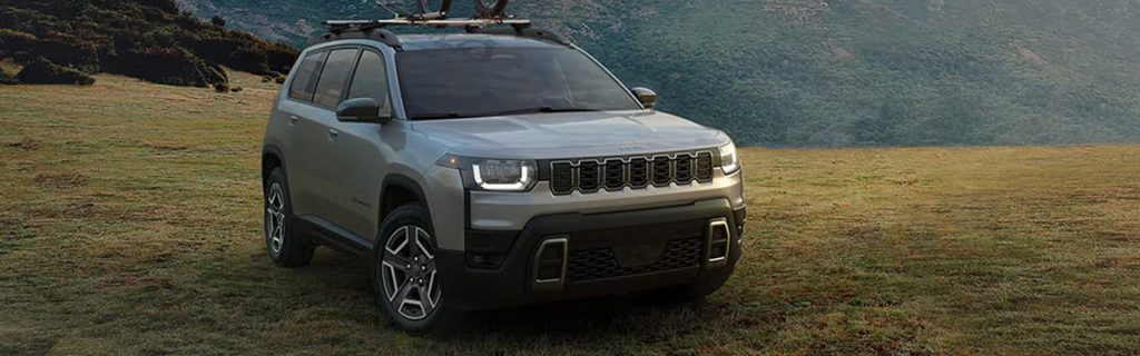 Silver Jeep SUV parked on a grassy field with hills in the background, showing front and side view