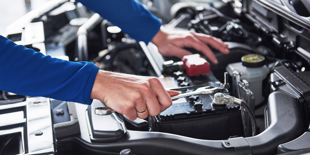 Close-up of a person working under the hood of a car, tightening the battery terminal with a wrench during a vehicle maintenance check.
