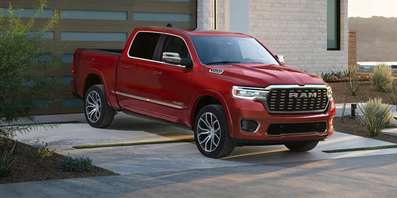 Front three-quarter view of a red RAM pickup truck parked on a modern driveway in front of a contemporary home, showcasing its bold grille, chrome accents, and alloy wheels.