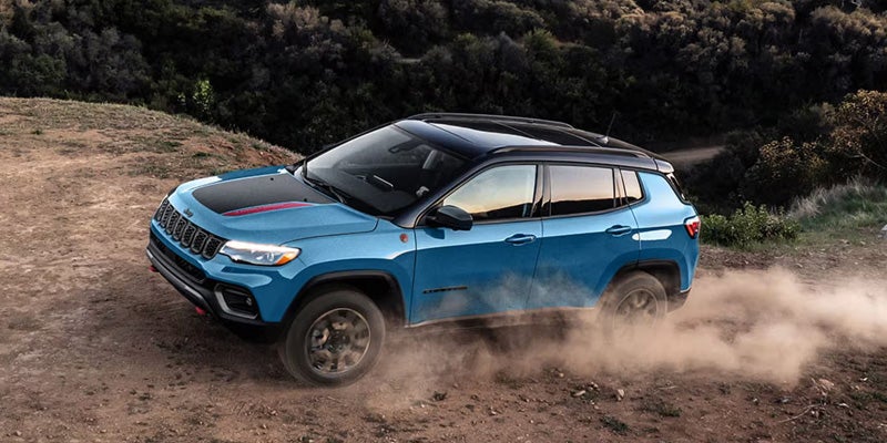 Blue Jeep Compass driving on a dusty dirt trail.