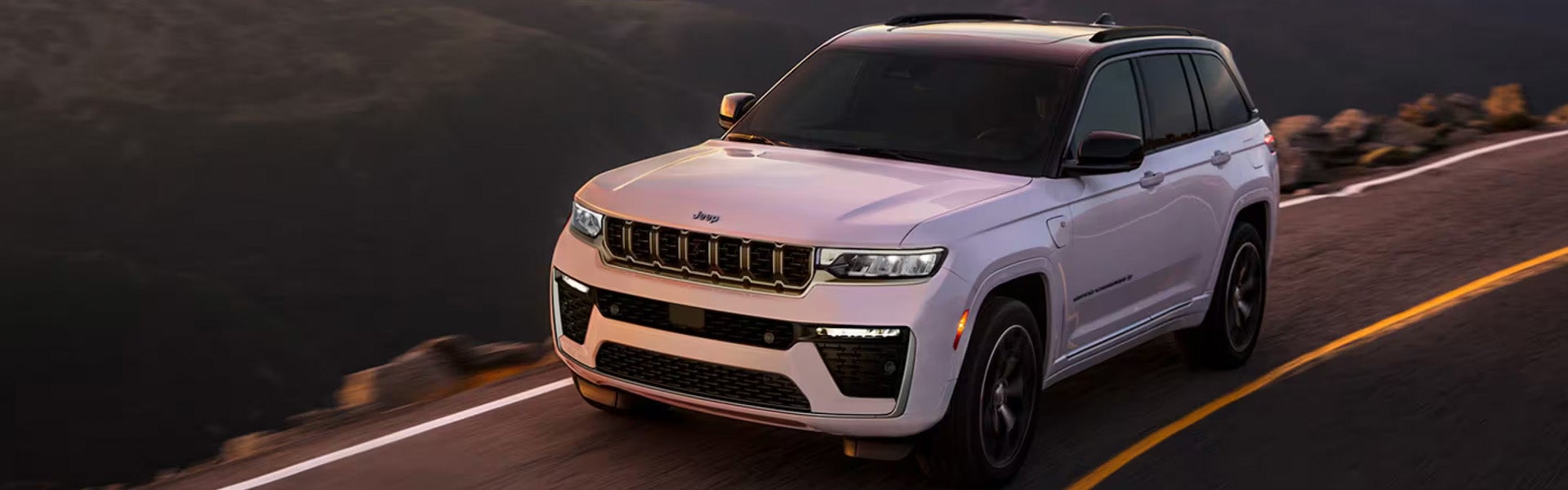White Jeep Grand Cherokee SUV driving on a scenic road.