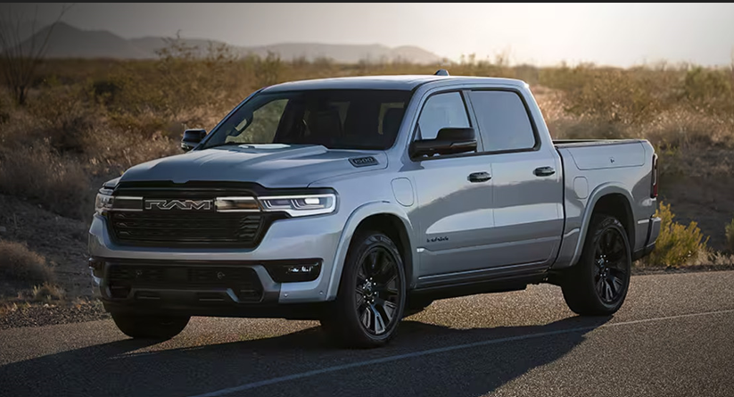 Silver RAM pickup truck parked on a paved road in a desert landscape at sunset.