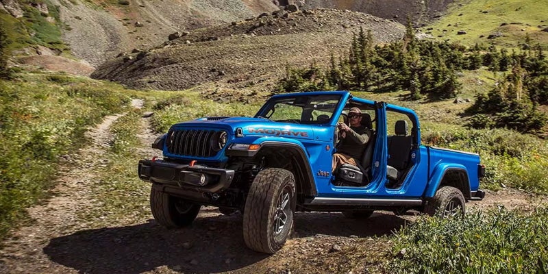 Blue Jeep Gladiator Rubicon driving off-road through a mountainous trail with rocky terrain.