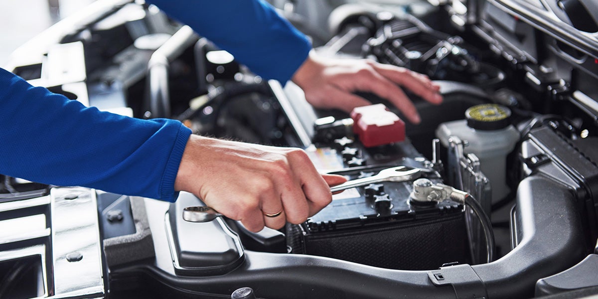 Technician using a wrench to service a car battery under the hood.
